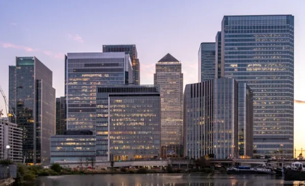 Skyline of Canary Wharf with modern skyscrapers reflected in the water at dusk.