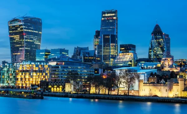 Skyline of London at dusk with modern skyscrapers and the River Thames in the foreground.