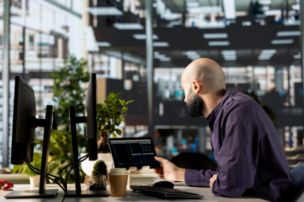 A person in a modern office setting works on cybersecurity tasks at a dual-monitor setup.