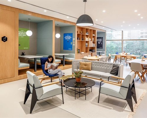 A modern office space with cozy seating areas, bookshelves, and a person reading on a chair.