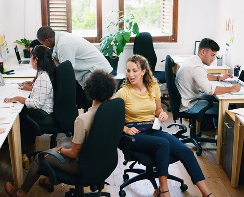 A busy office scene with several people working at desks and collaborating.