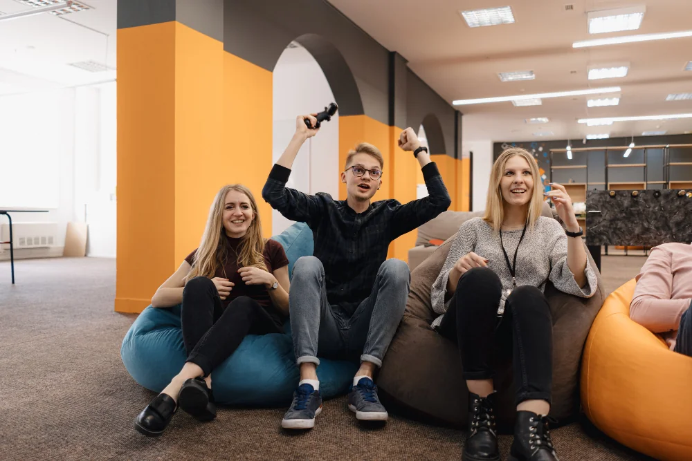 Three people enjoying a relaxed moment on bean bags in a modern office space.