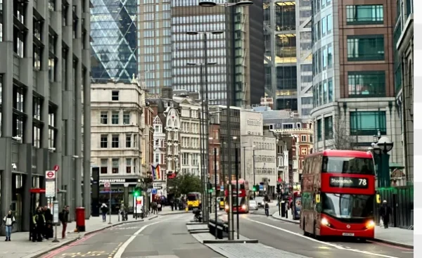 A busy street in Liverpool with modern and historic buildings, featuring a classic red double-decker bus.