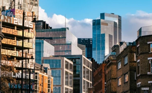 Shoreditch cityscape featuring modern and older buildings under a blue sky with clouds.
