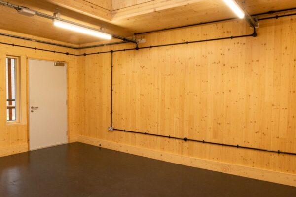 An empty room with wooden walls, visible wiring, and a closed white door at Abbott Road 384, London.