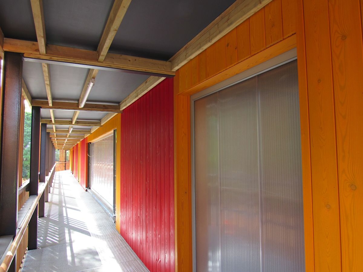 A long corridor with vibrant orange and red wooden walls and a metal walkway at Abbott Road 384, London.