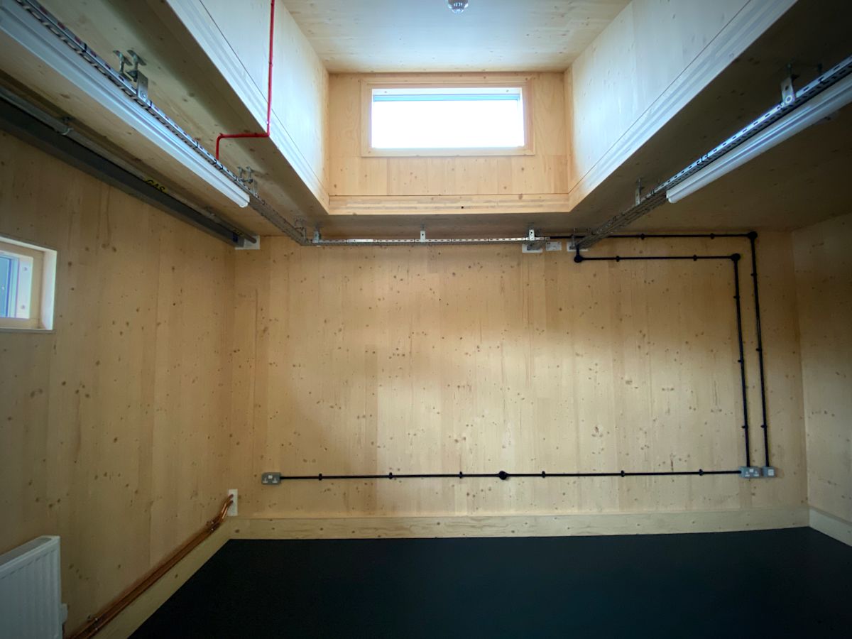 A wooden interior room with visible piping and a small rectangular window at Abbott Road 384, London.