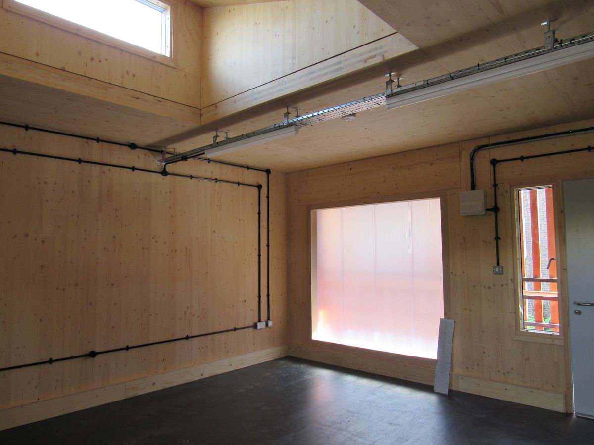 Interior of a wooden room with exposed pipes and large frosted windows at Abbott Road 384, London.