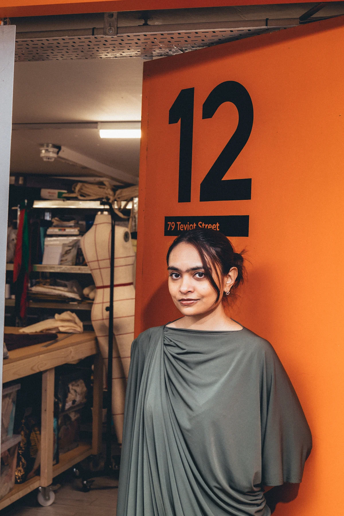 Person standing in front of an orange wall with the number 12 and address "79 Teviot Street" in a workshop setting.