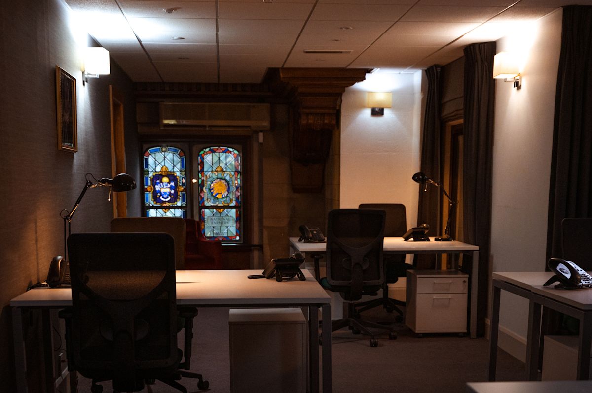 A dimly lit office space with desks, chairs, and a stained glass window in the background at Aldermanbury 20 21, London.