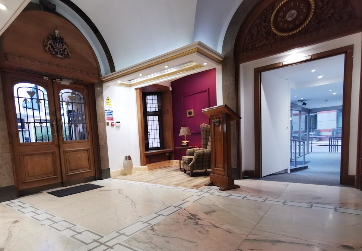 The entrance hall of a London building with marble flooring, wooden doors, and a small seating area.
