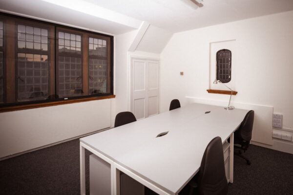 A modern office space with a large desk and multiple chairs, located in Aldermanbury, London.
