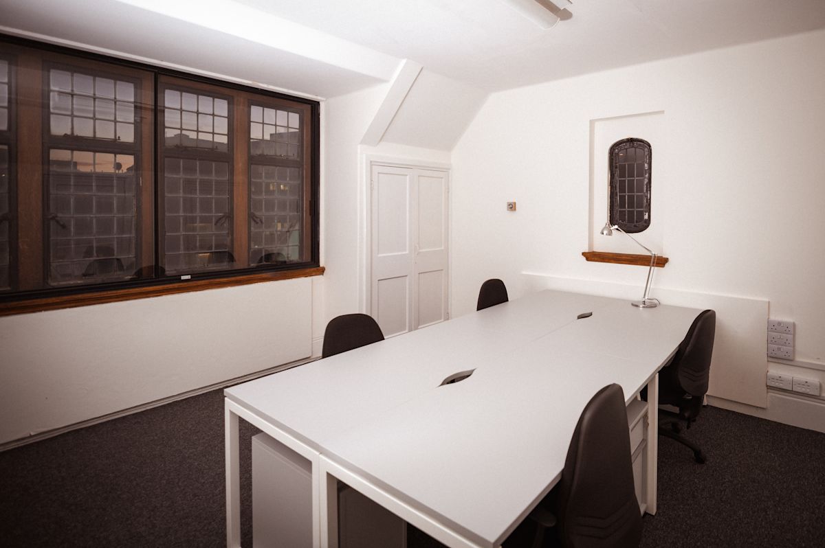 A modern office space with a large desk and multiple chairs, located in Aldermanbury, London.