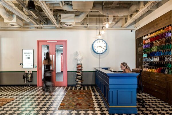 A modern, stylish lobby featuring a blue reception desk, a wall clock, and colorful yarn shelves at Appold Street 9, London.
