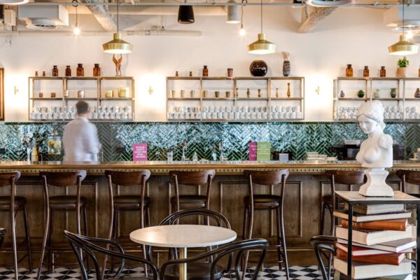 A stylish bar interior at Appold Street 9 London, featuring a wooden counter, green tiled backsplash, and decorative bust.