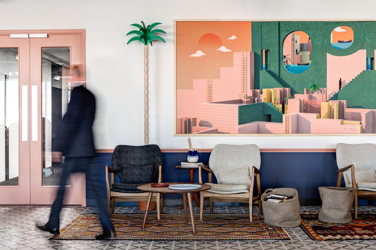A blurred man walks through a stylish interior with modern chairs, a decorative palm tree, and vibrant wall art.