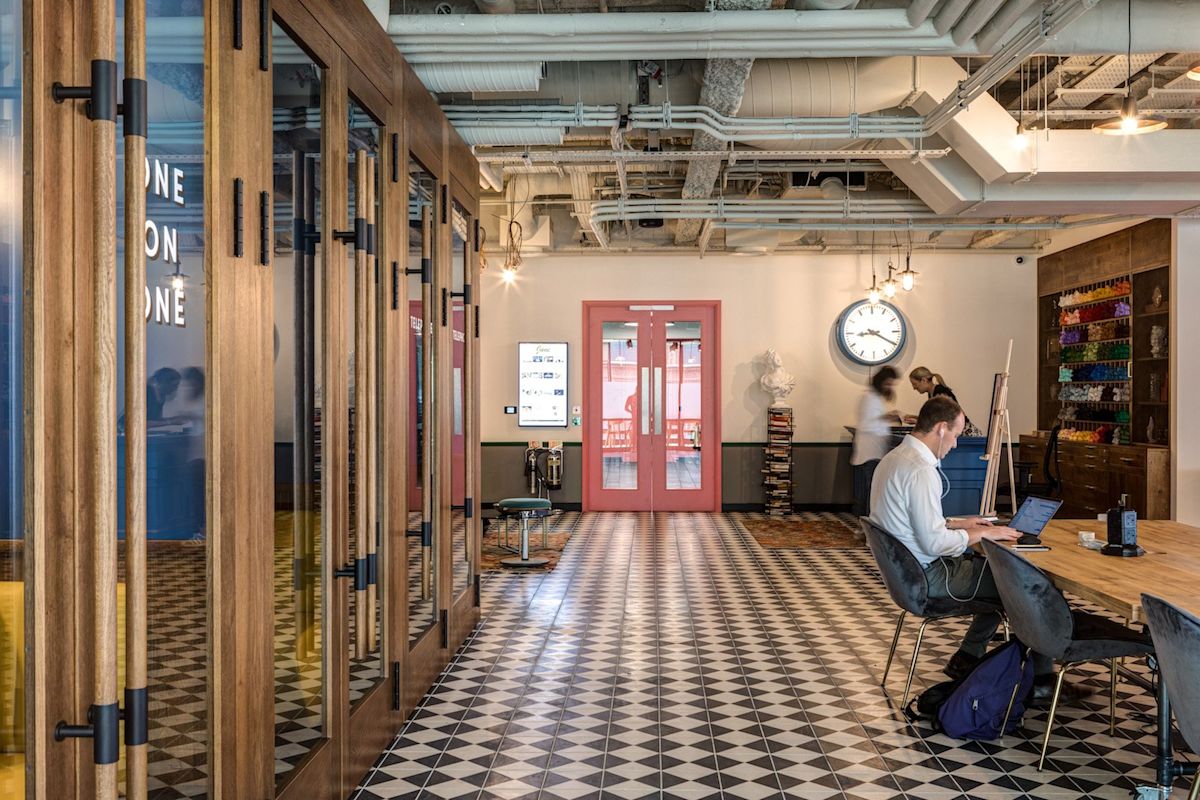 A modern office space on Appold Street 9, London, featuring a person working at a wooden table with vibrant decor and geometric flooring.