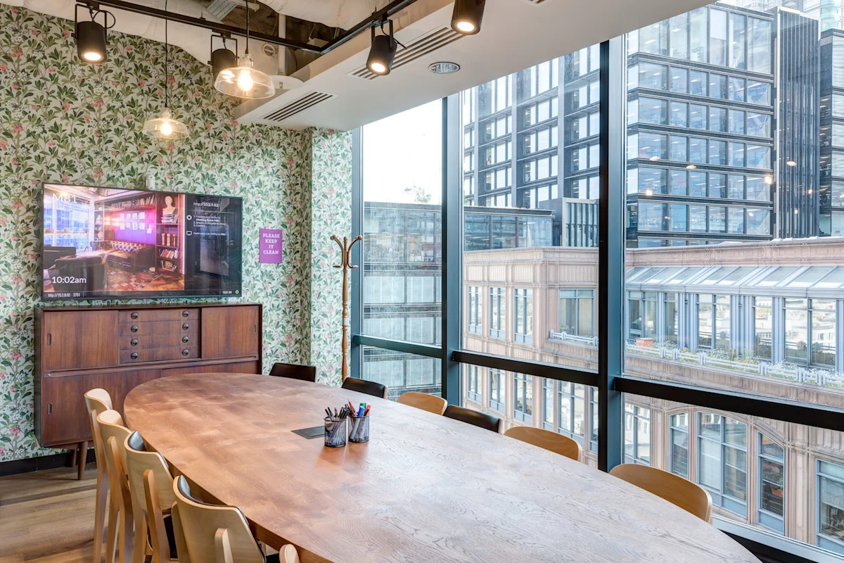 Modern conference room with a wooden table, floral wallpaper, and large windows overlooking London buildings.