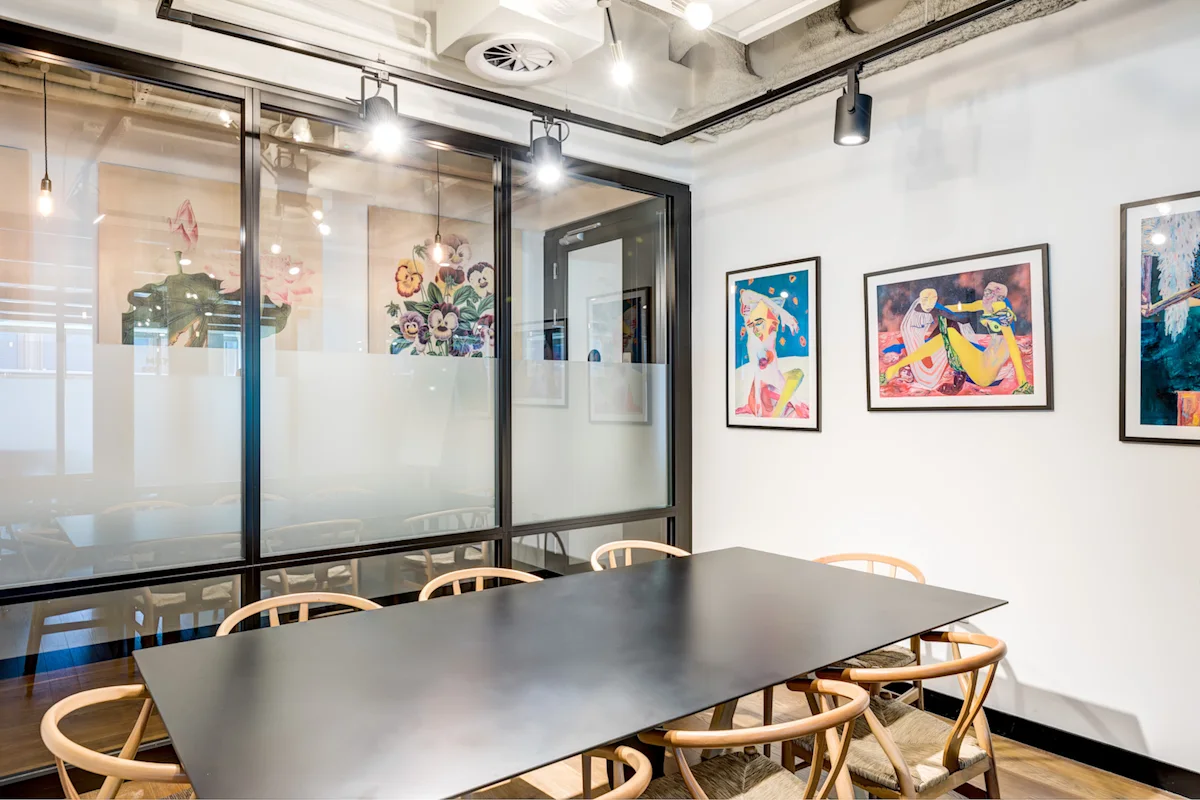 A modern meeting room with a black table, wooden chairs, and colorful artwork on the walls.