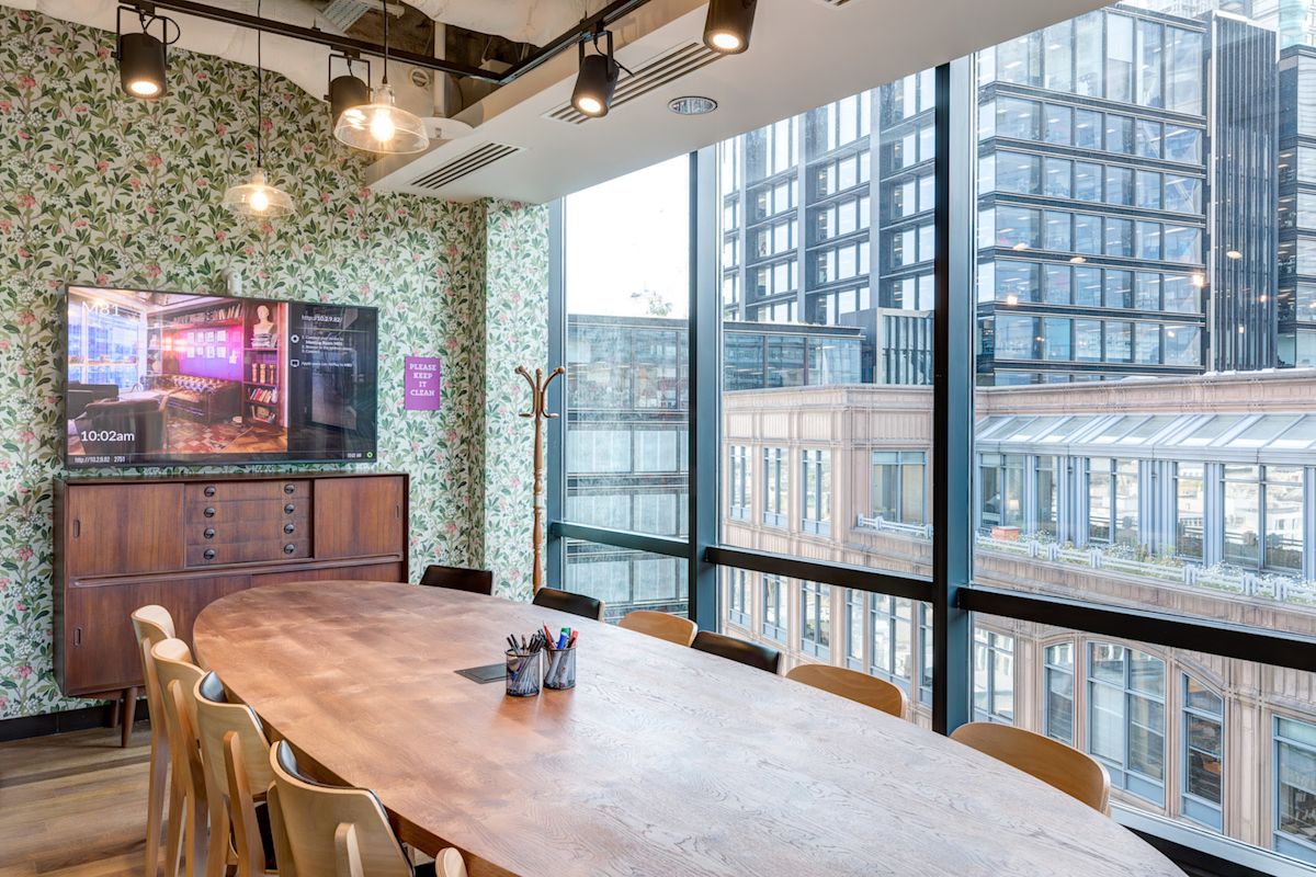 A modern meeting room with a large wooden table, surrounded by windows offering a view of London buildings.