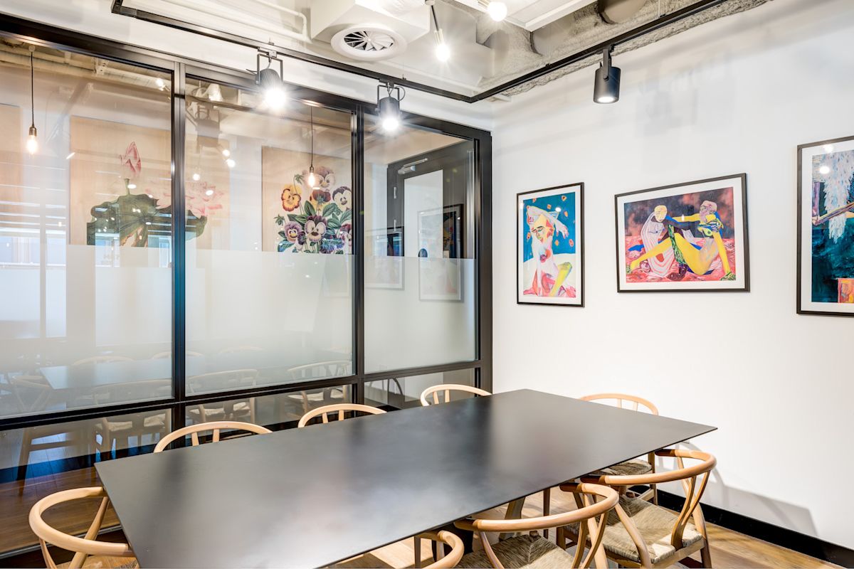 A modern meeting room with a large table, wooden chairs, and colorful artwork on the walls.