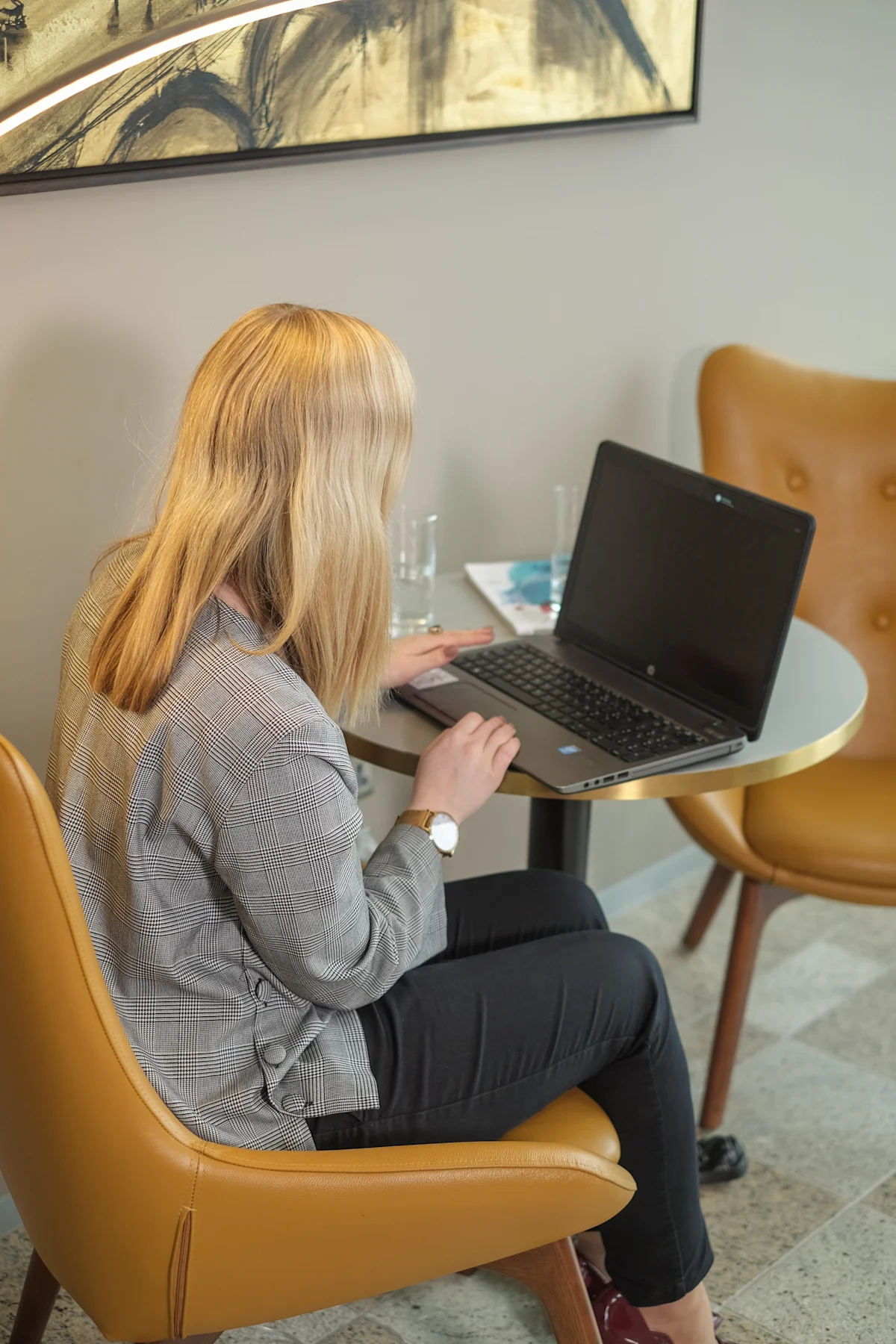 A woman sitting at a small table working on a laptop in an office setting.