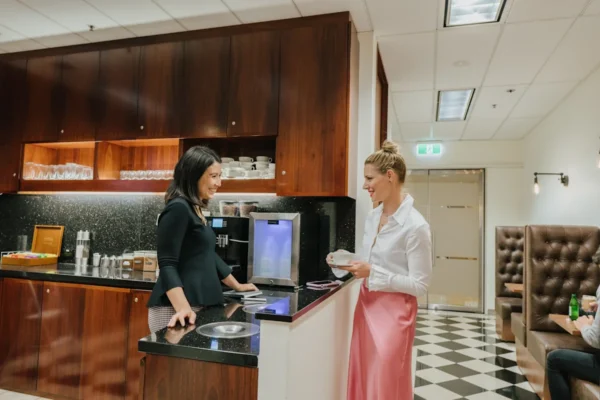 Two women are smiling and talking in a modern kitchen area at Bank Street 40, London.