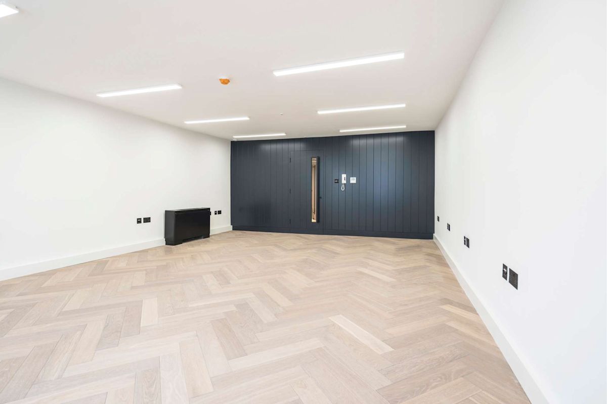 An empty room with light wooden herringbone flooring and a dark blue feature wall at Berwick Street 30, London.