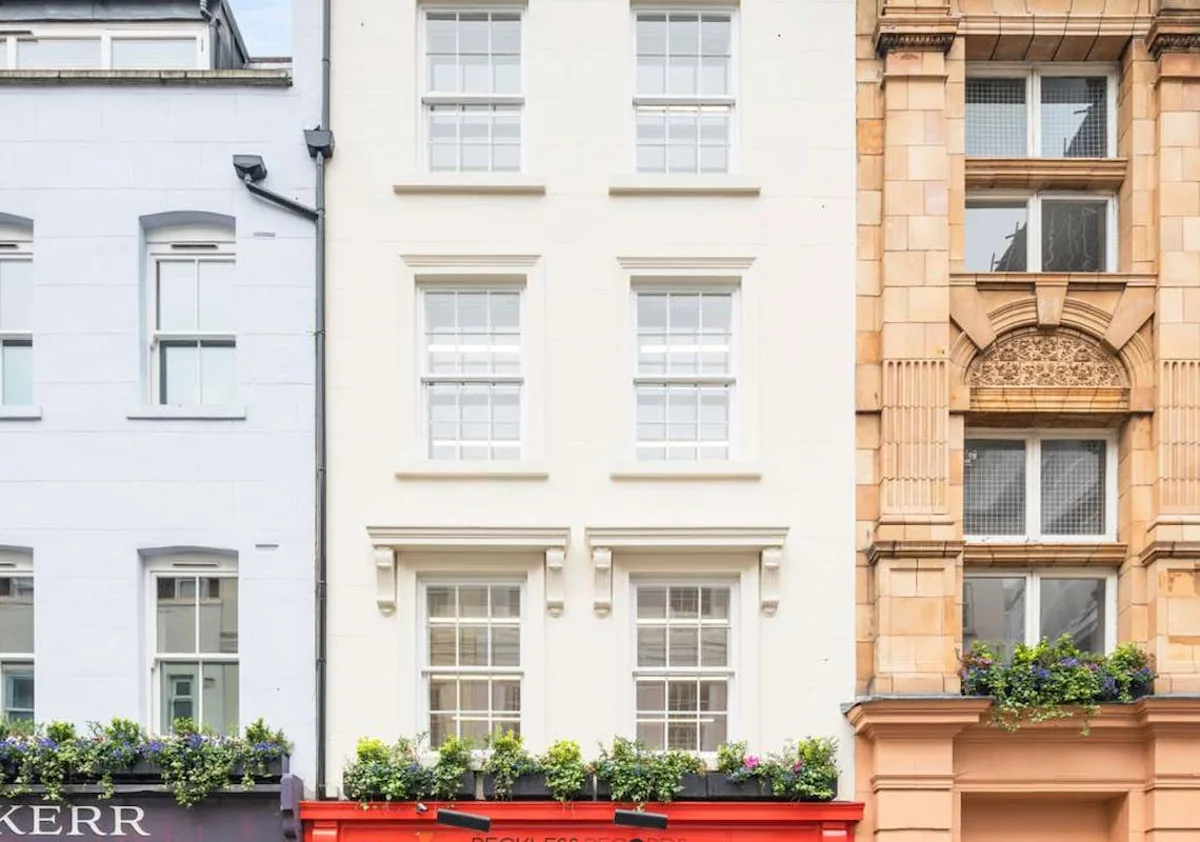Facade of buildings on Berwick Street, London, with white and beige exteriors adorned with flower boxes.