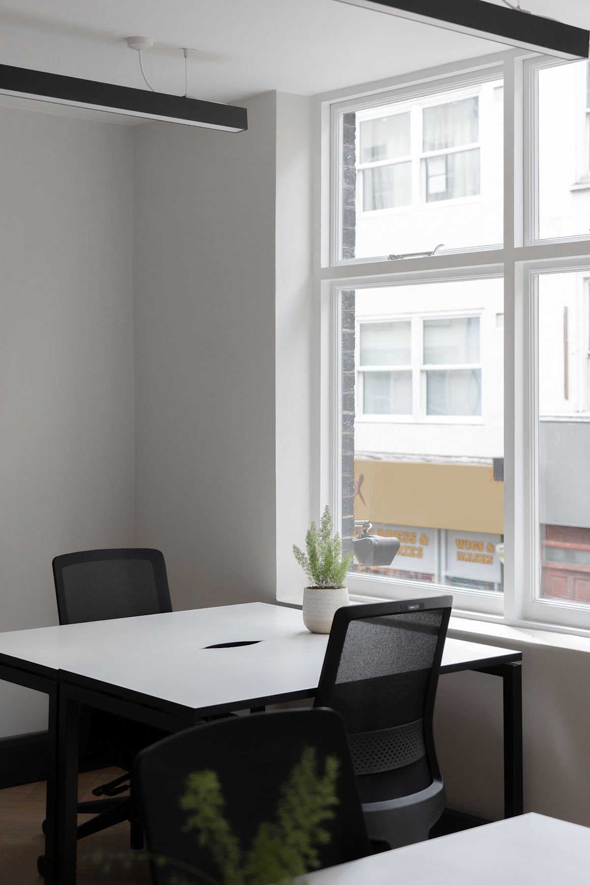 A modern office space with white desks and chairs near a large window with a view of Berwick Street, London.
