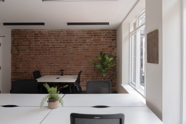 A modern office space with white desks, black chairs, and a brick accent wall.