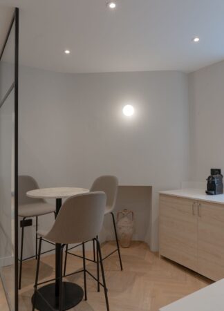 A modern kitchen corner with a small table, two chairs, and a countertop with a coffee machine.
