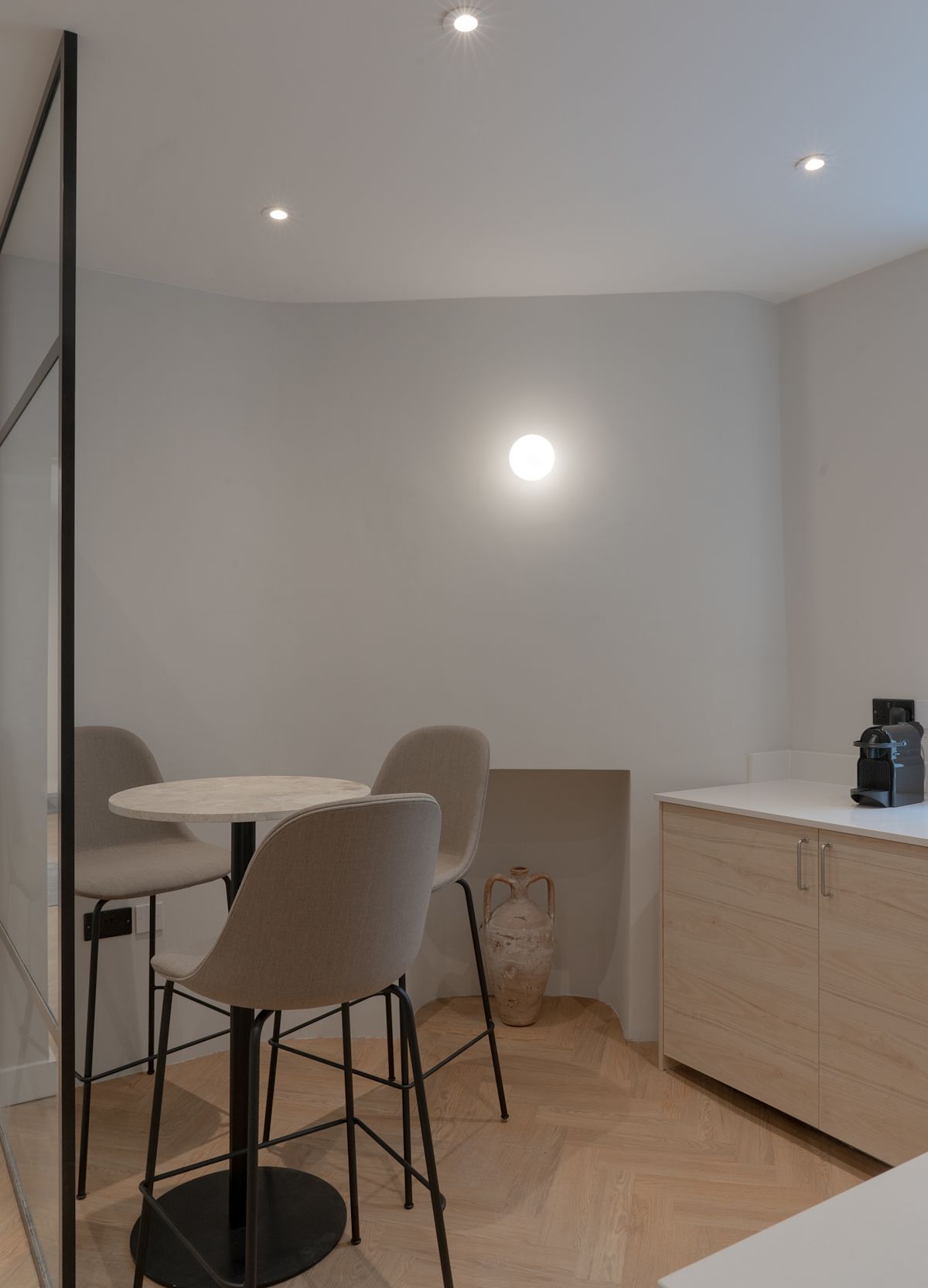 A modern kitchen corner with a small table, two chairs, and a countertop with a coffee machine.