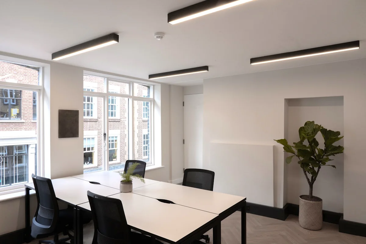 A modern office space with large windows, minimalist furniture, and a potted plant.