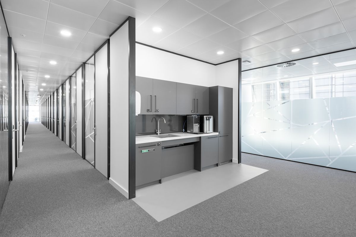A modern office corridor at Bishopsgate 100 in London, featuring a small kitchenette with gray cabinets.