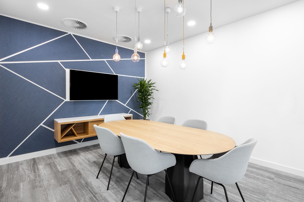 A modern conference room at 100 Bishopsgate, London, featuring a wooden table, grey chairs, geometric wall design, and hanging light bulbs.