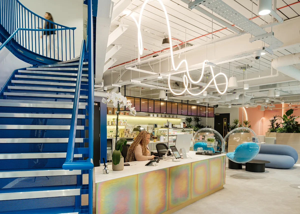 A modern, vibrant office interior at Bishopsgate 199 London with a blue staircase, colorful reception desk, and contemporary seating.