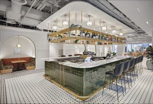 A modern bar with green tiled front and overhead shelving filled with bottles and lights at Bishopsgate 22 London.