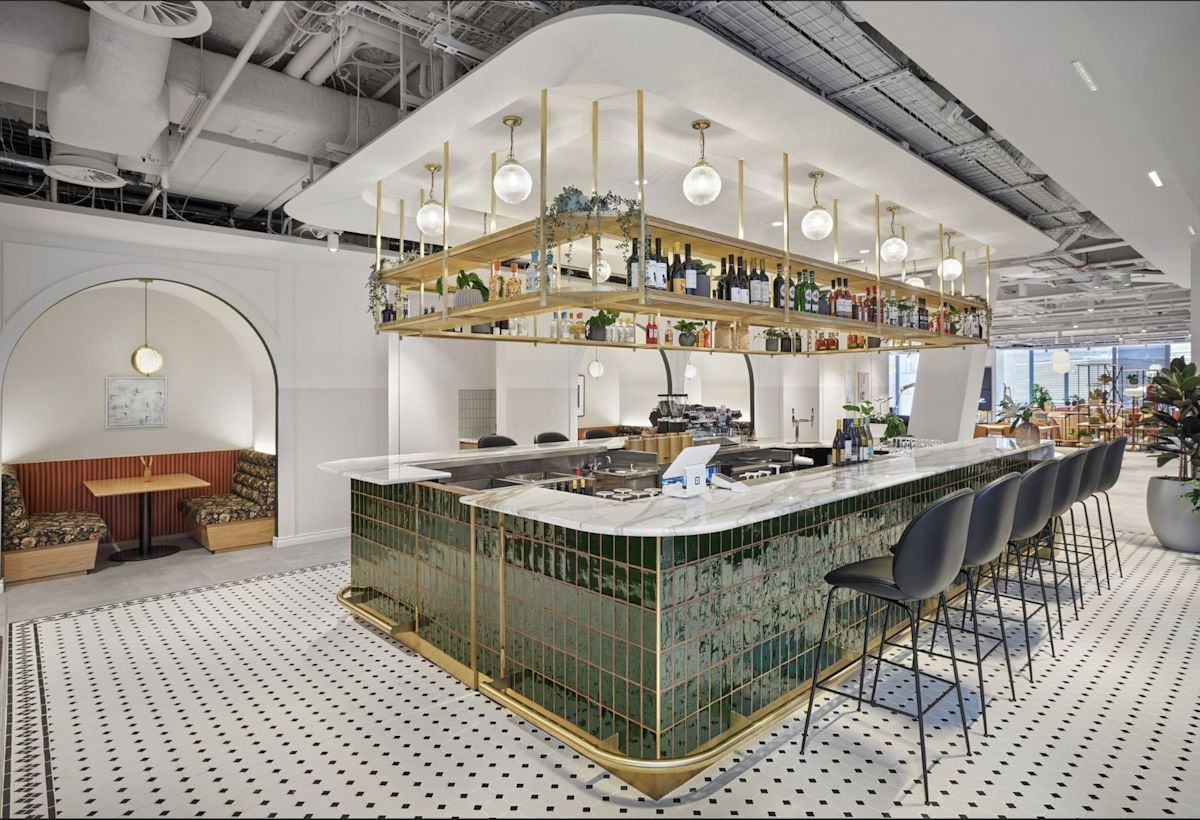 A modern bar with green tiled front and overhead shelving filled with bottles and lights at Bishopsgate 22 London.