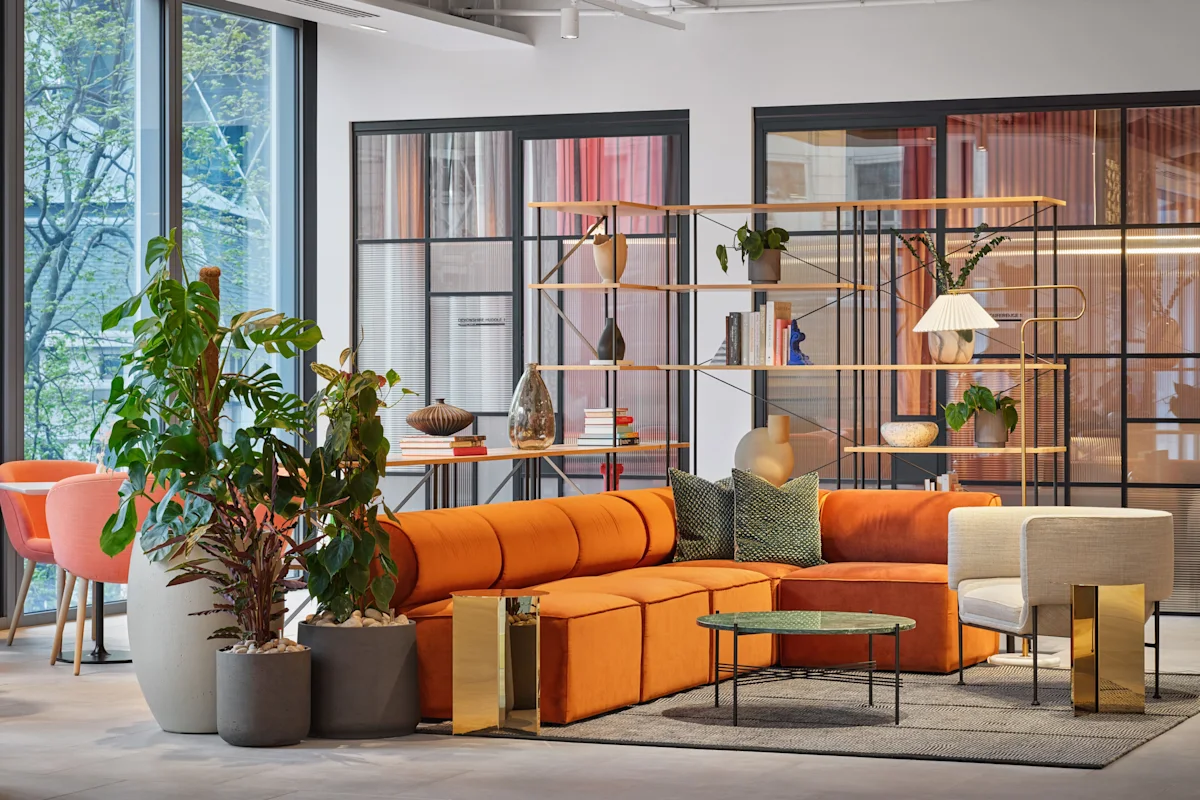 Modern lounge area with an orange sofa, plants, and stylish decor in an office setting.