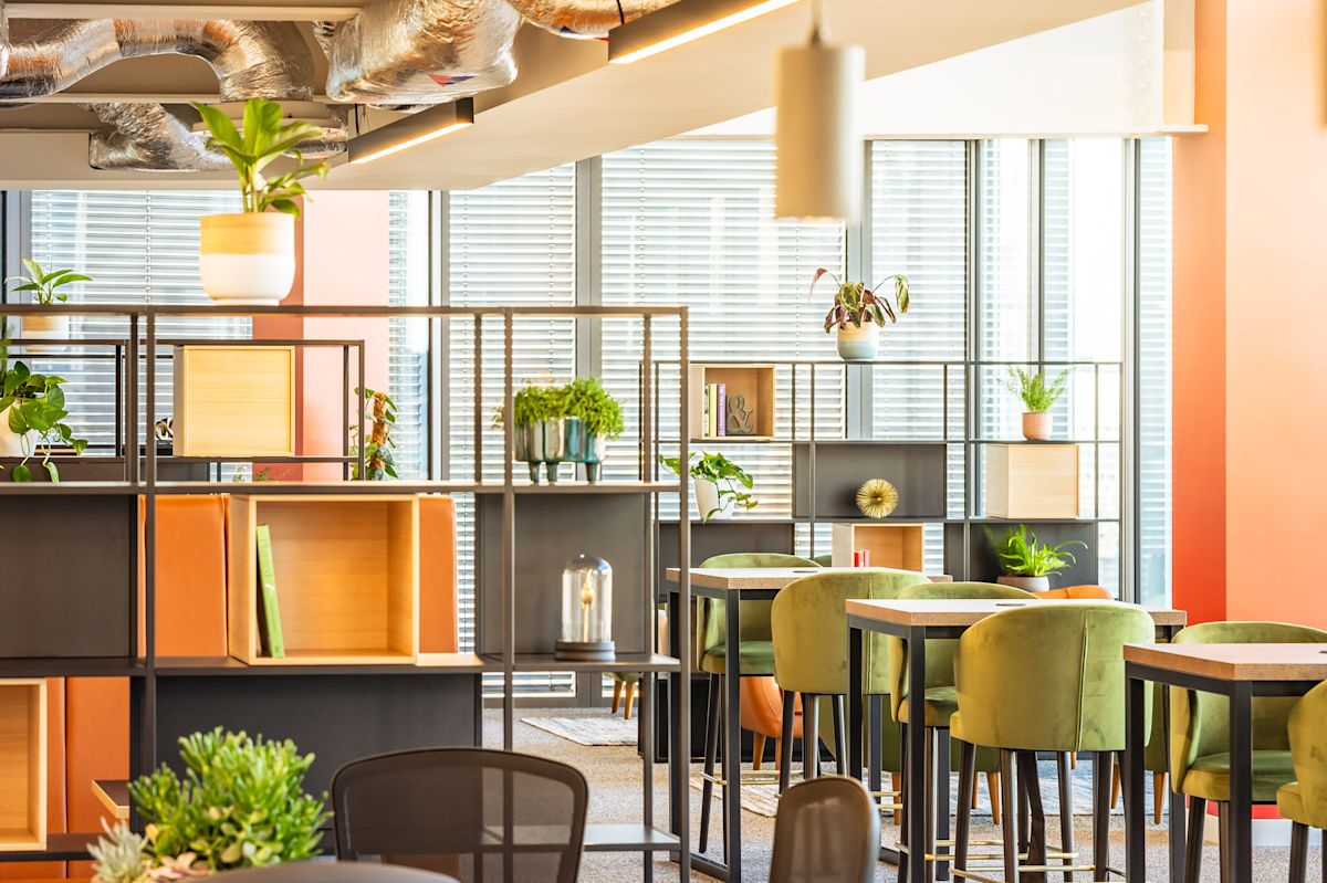 A modern and bright office space with green chairs, plants, and large windows at 22 Bishopsgate, London.