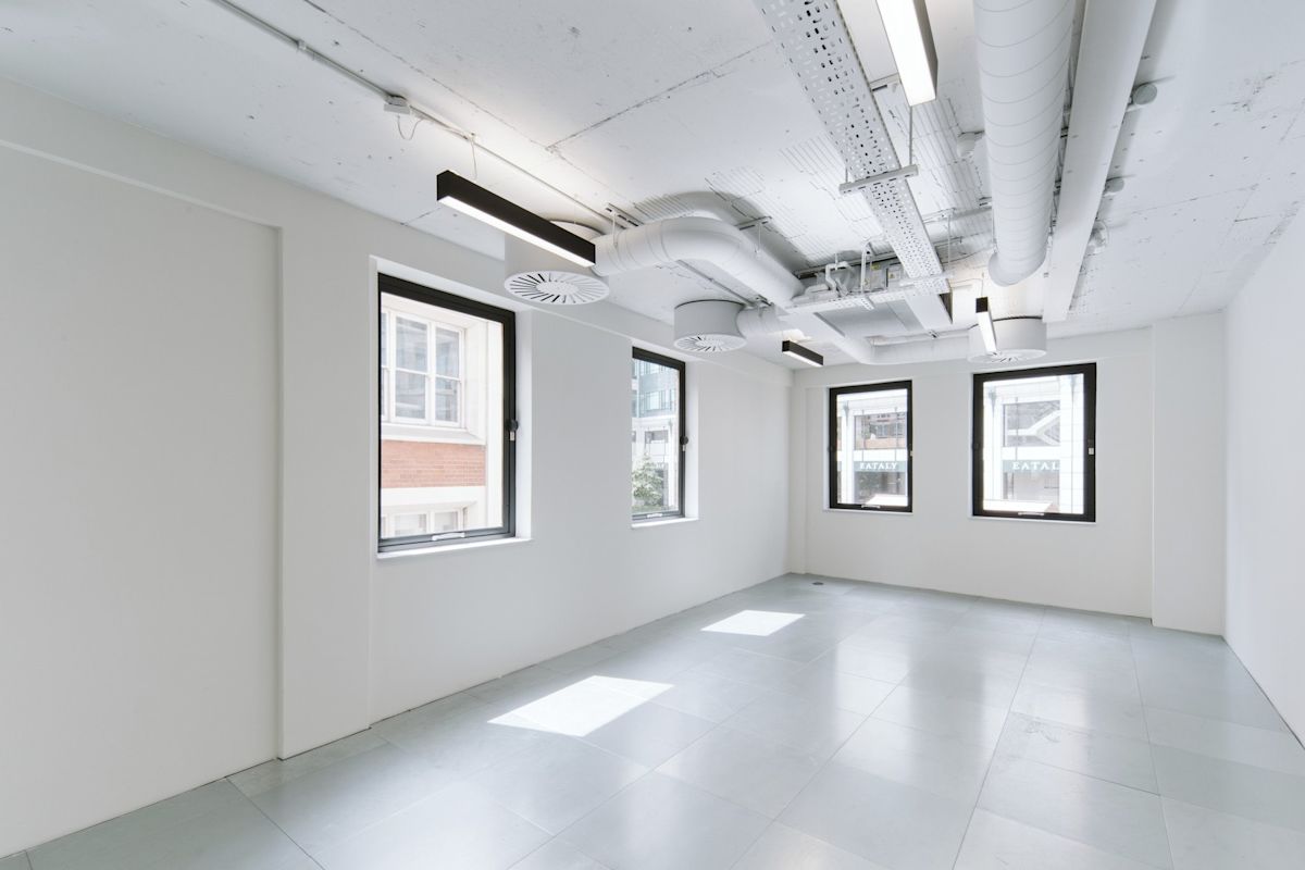 An empty modern office space with large windows and exposed ceiling ductwork at 222 Bishopsgate, London.