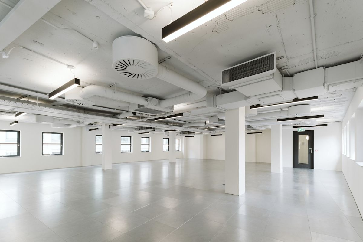 The image shows an empty, modern office space in Bishopsgate 222 B London with exposed ceilings and large windows.