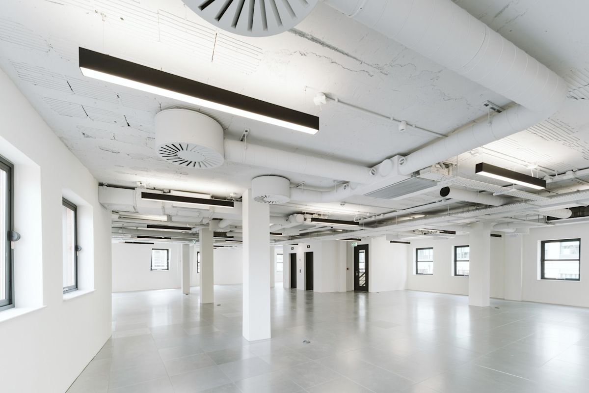 A spacious, modern industrial interior of an office space at 222 Bishopsgate, London, with exposed ceilings and large windows.
