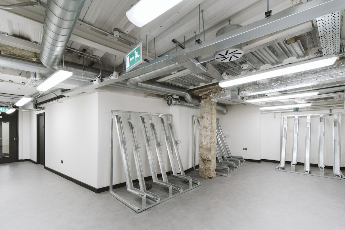 Modern bicycle storage area with metal racks and exposed ceiling pipes at Bishopsgate 222 B, London.