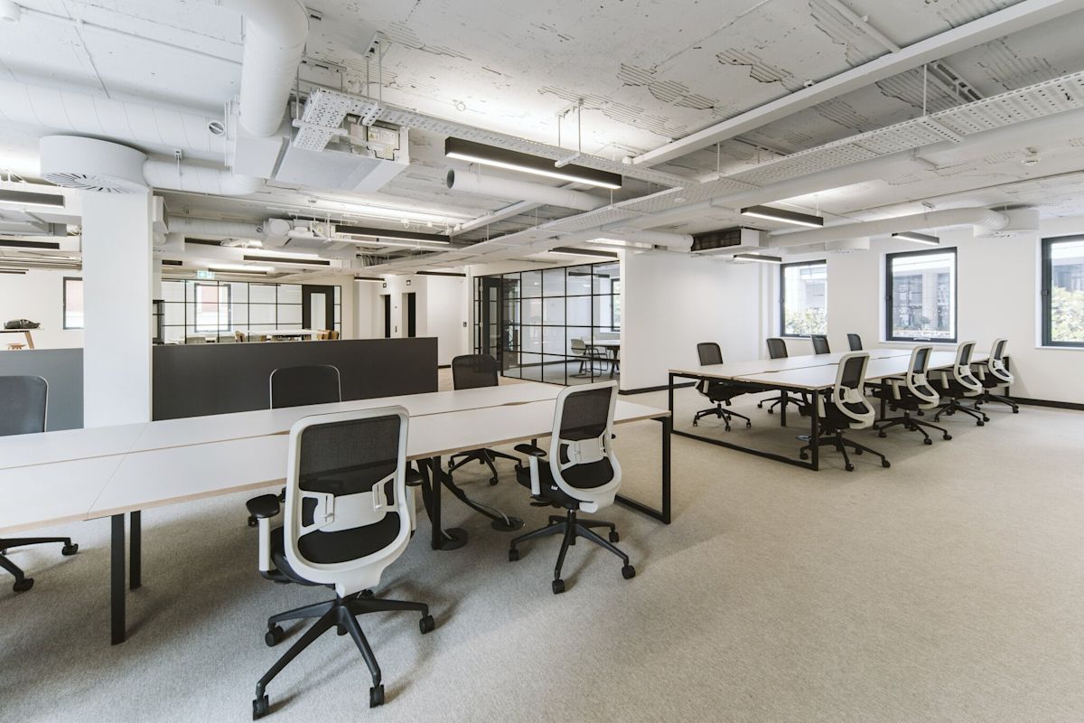 A modern open-plan office space with white walls and multiple desks and chairs.