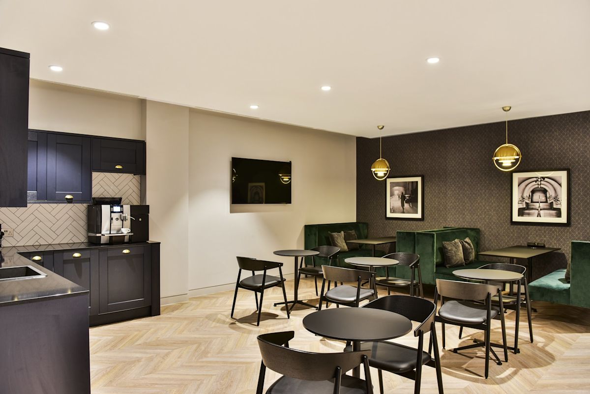 Modern break room at 288 Bishopsgate, London, featuring dark cabinetry, green seating, and round tables.
