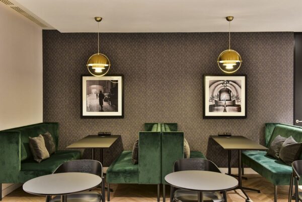 Modern seating area with green velvet booths, round tables, and framed photographs on a patterned wall at Bishopsgate 288, London.