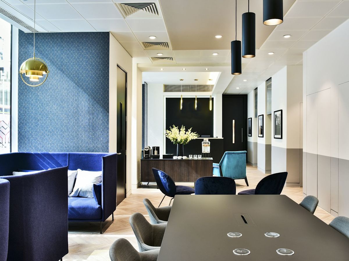 Modern office lounge area with blue seating, a long table, and decorative lighting at Bishopsgate 288, London.