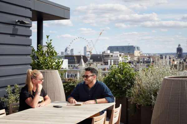 Two people enjoy a conversation at a rooftop terrace with a cityscape view featuring the London Eye.